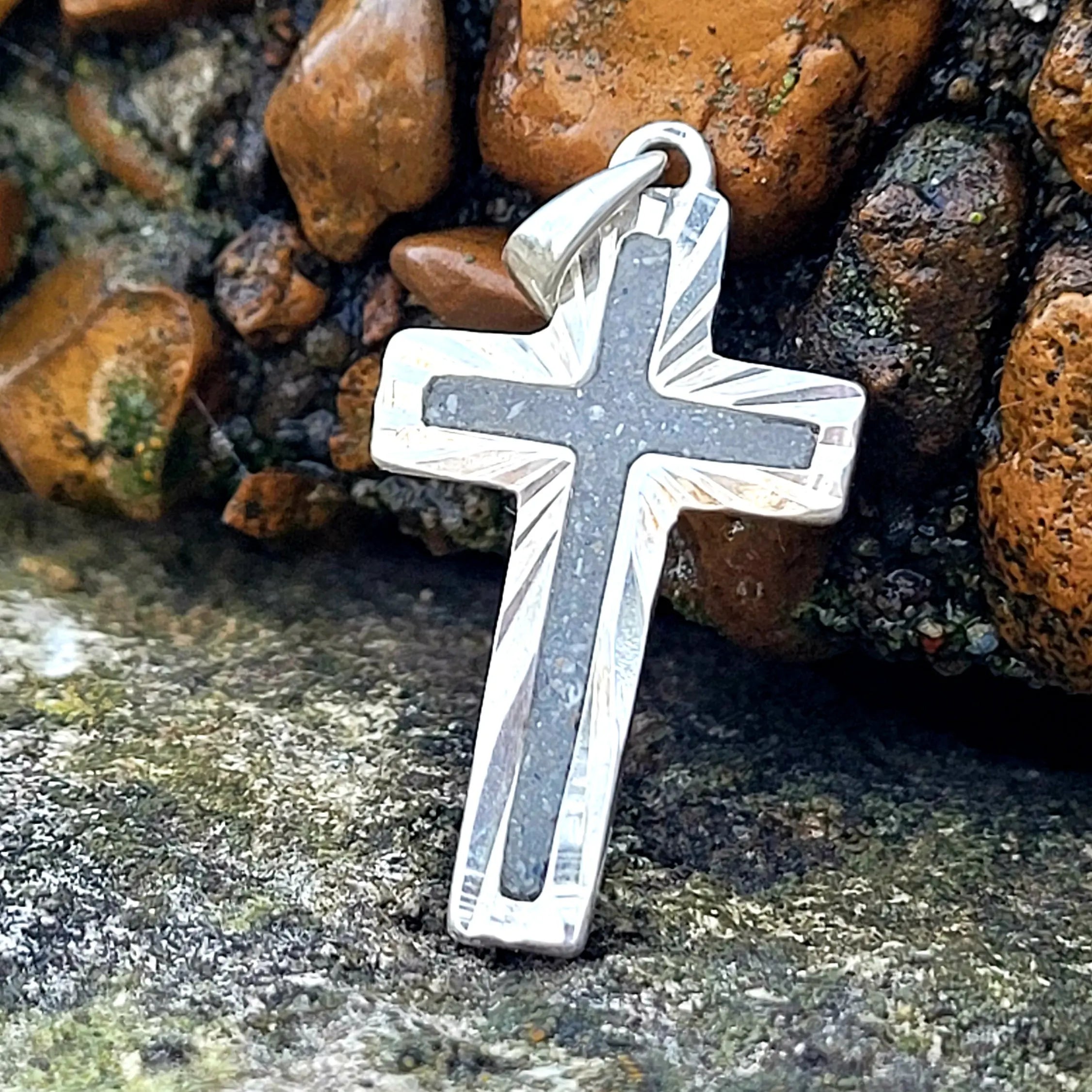 Sterling silver cross pendant with grey stone inlay on a mossy rock surface. Religious jewelry, handcrafted.