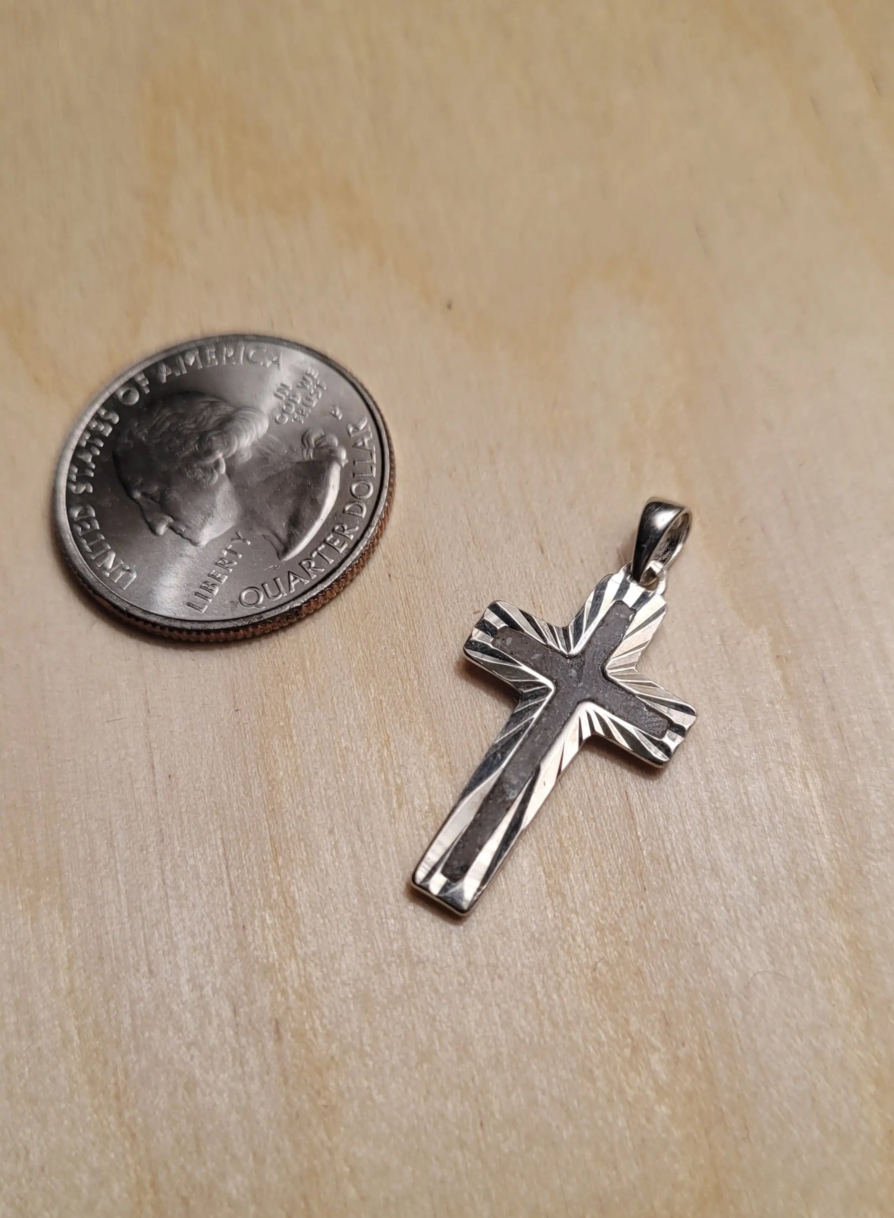 Sterling silver cross pendant with textured design next to a United States quarter for size comparison on a wood surface.