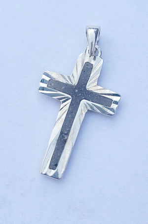 Sterling silver cross pendant with dark stone inlay, viewed close-up on a white background.