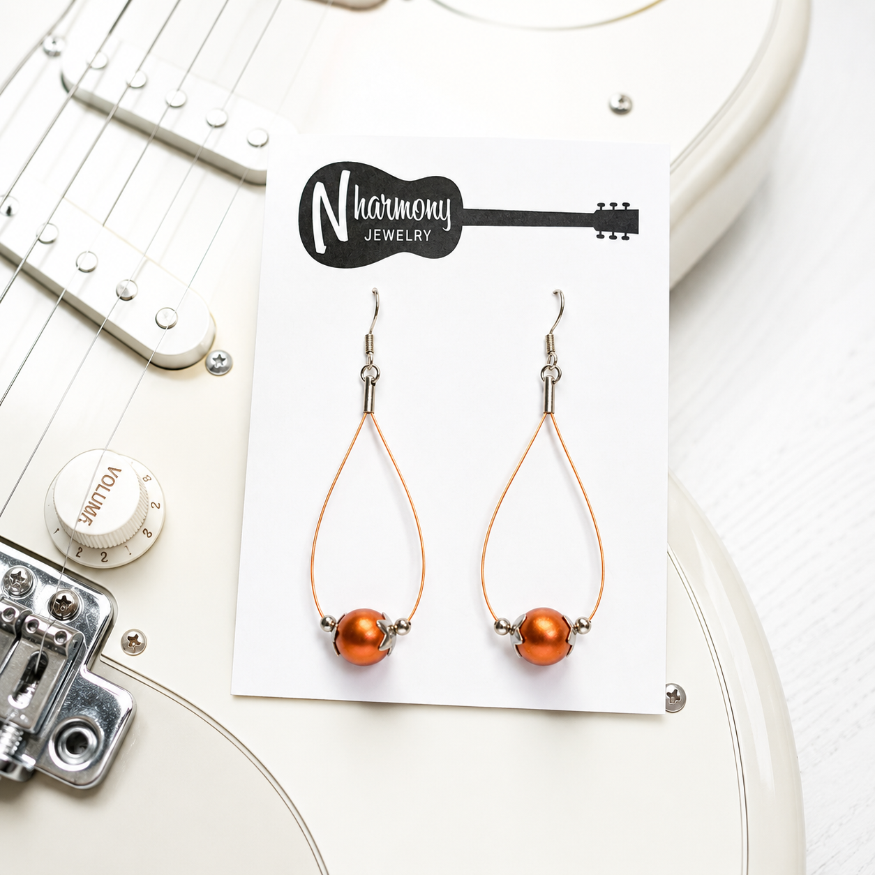 Orange teardrop earrings on a Harmony Jewelry card with a guitar in the background