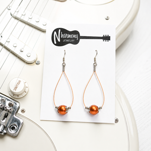 Orange teardrop earrings on a Harmony Jewelry card with a guitar in the background