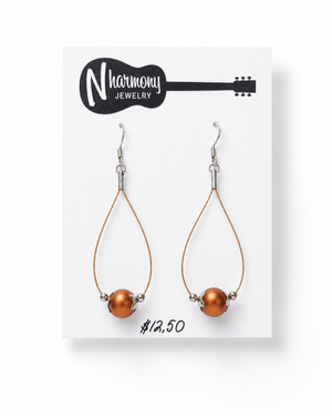 Pair of teardrop-shaped earrings with orange beads on a N'Harmony Jewelry card.