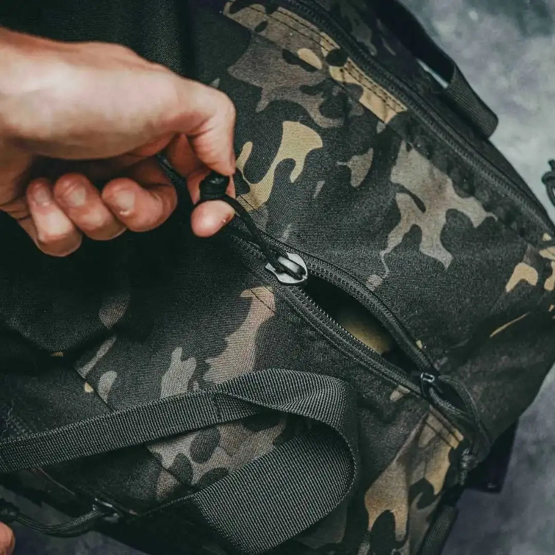 Camouflage duffle bag with a hand opening a zipper.