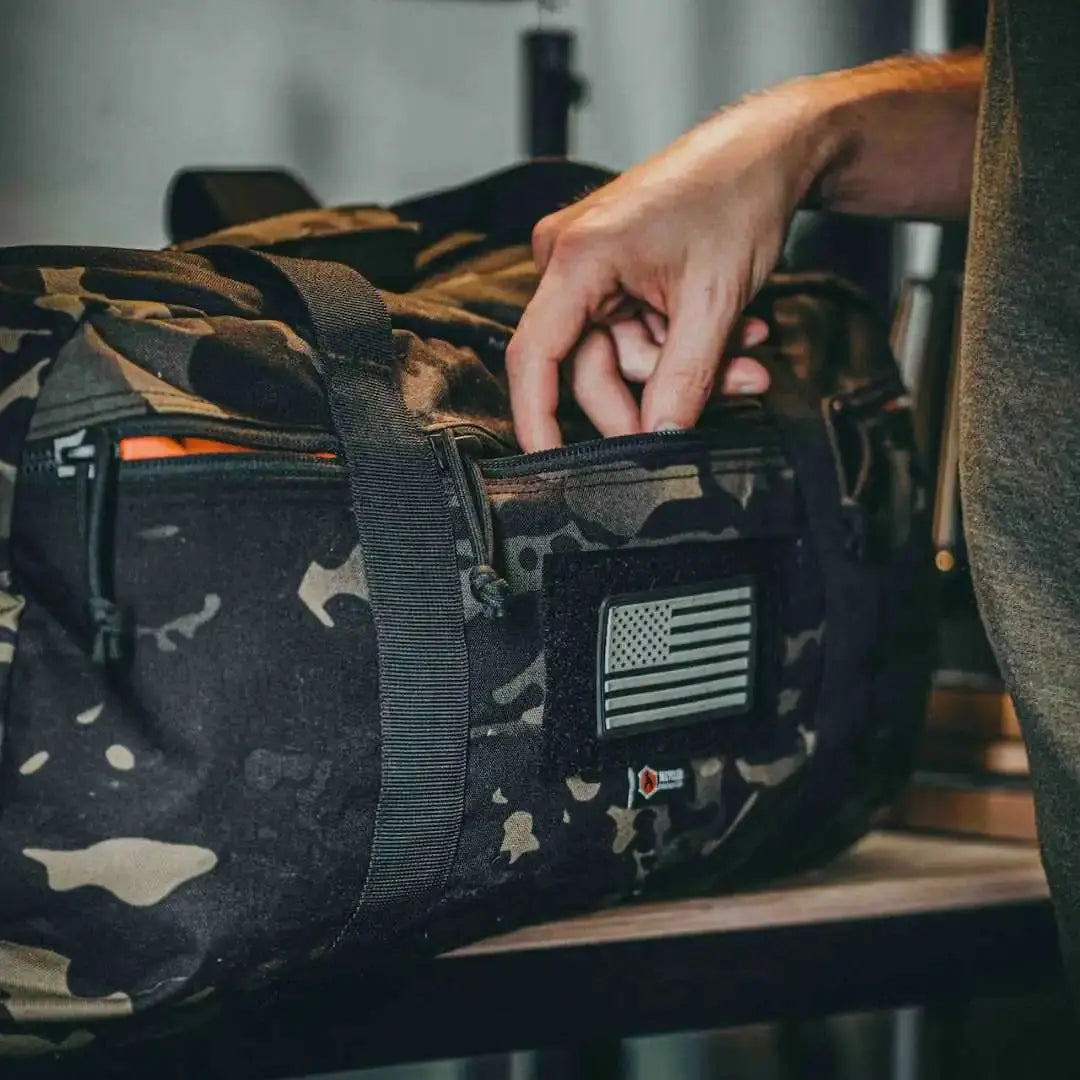 Camo duffle bag with American flag patch being accessed by a hand.