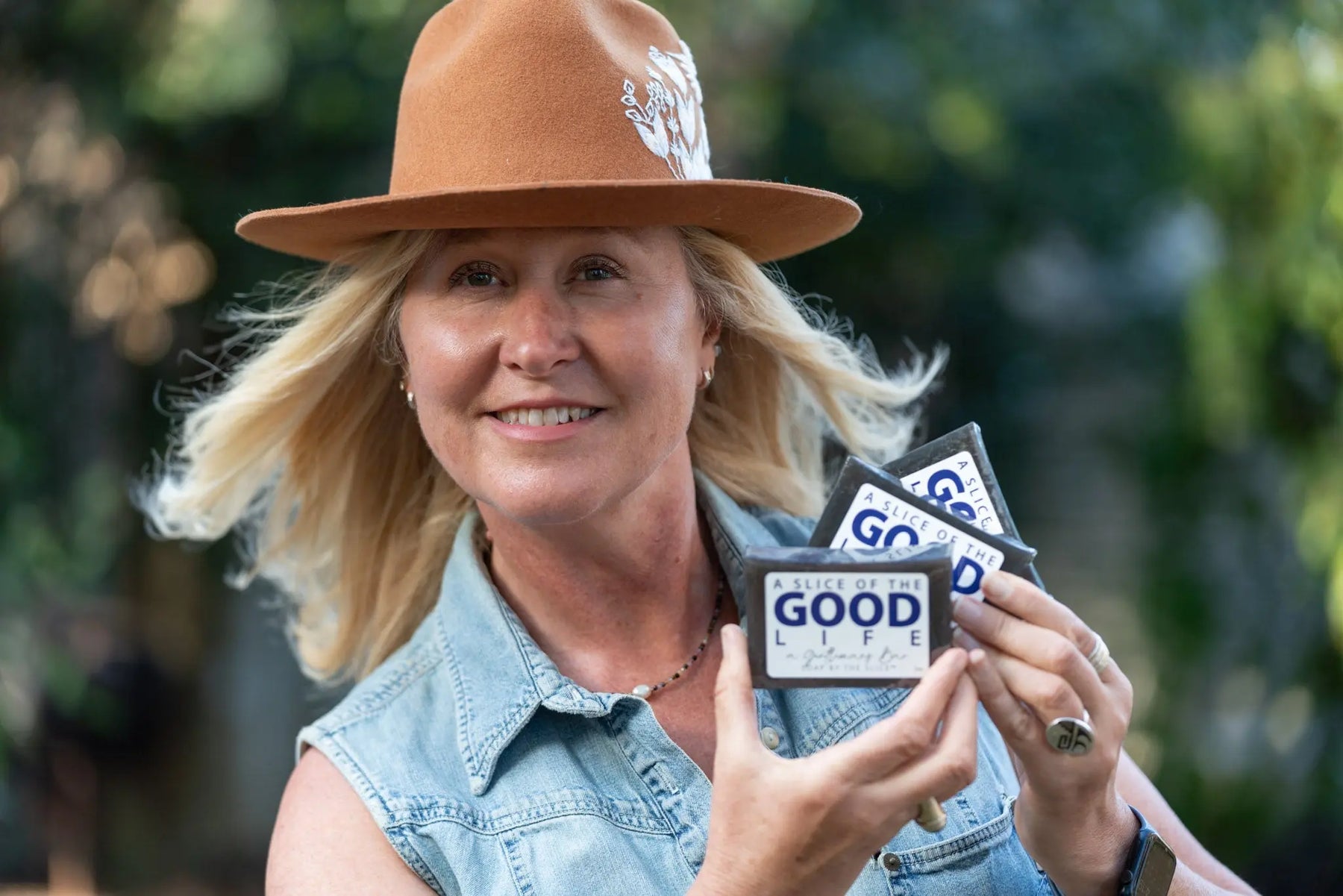 Woman in a hat holding two bars of "A Slice of the Good Life" soap.