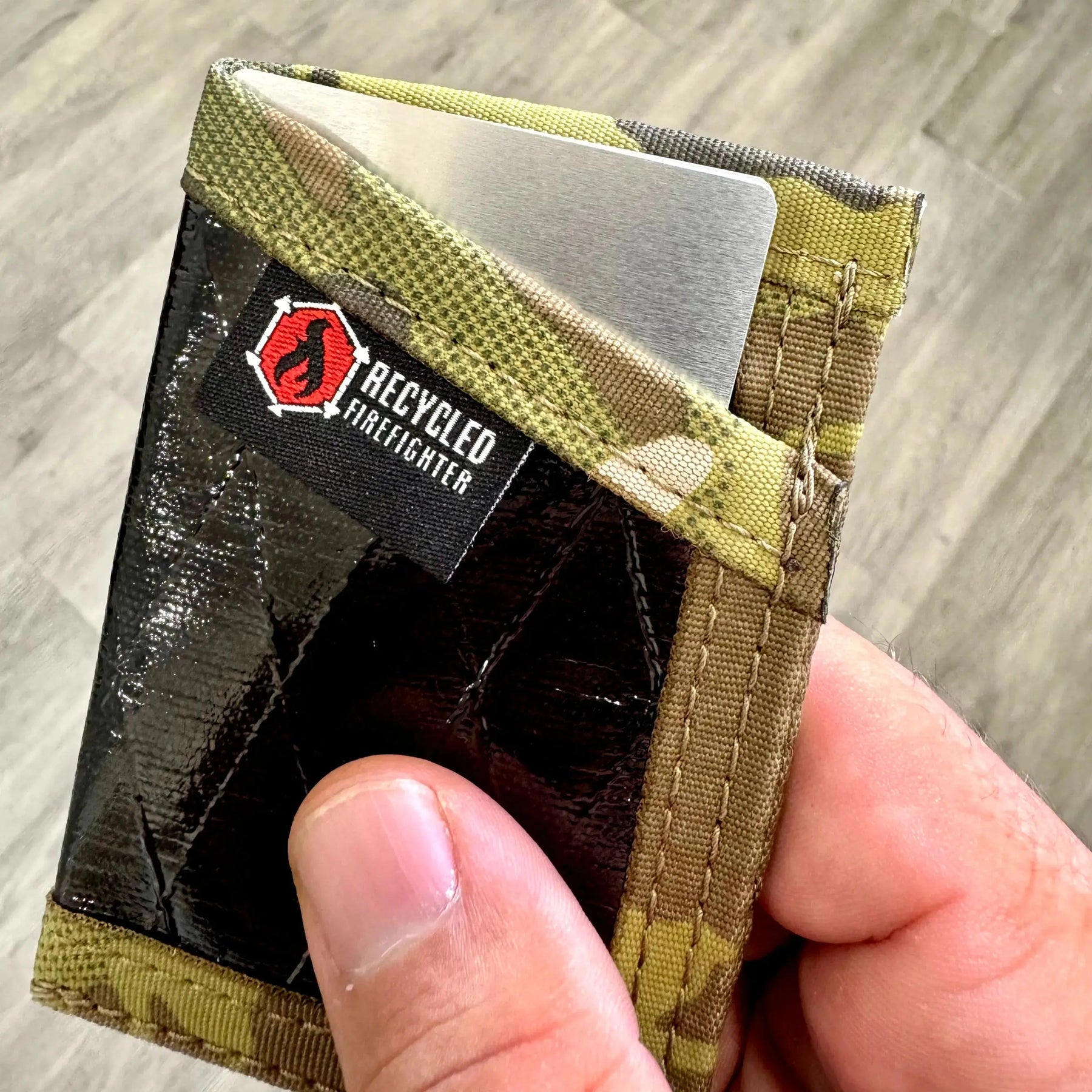 Thin aluminum RFID blocking card with camouflage trim held in hand.