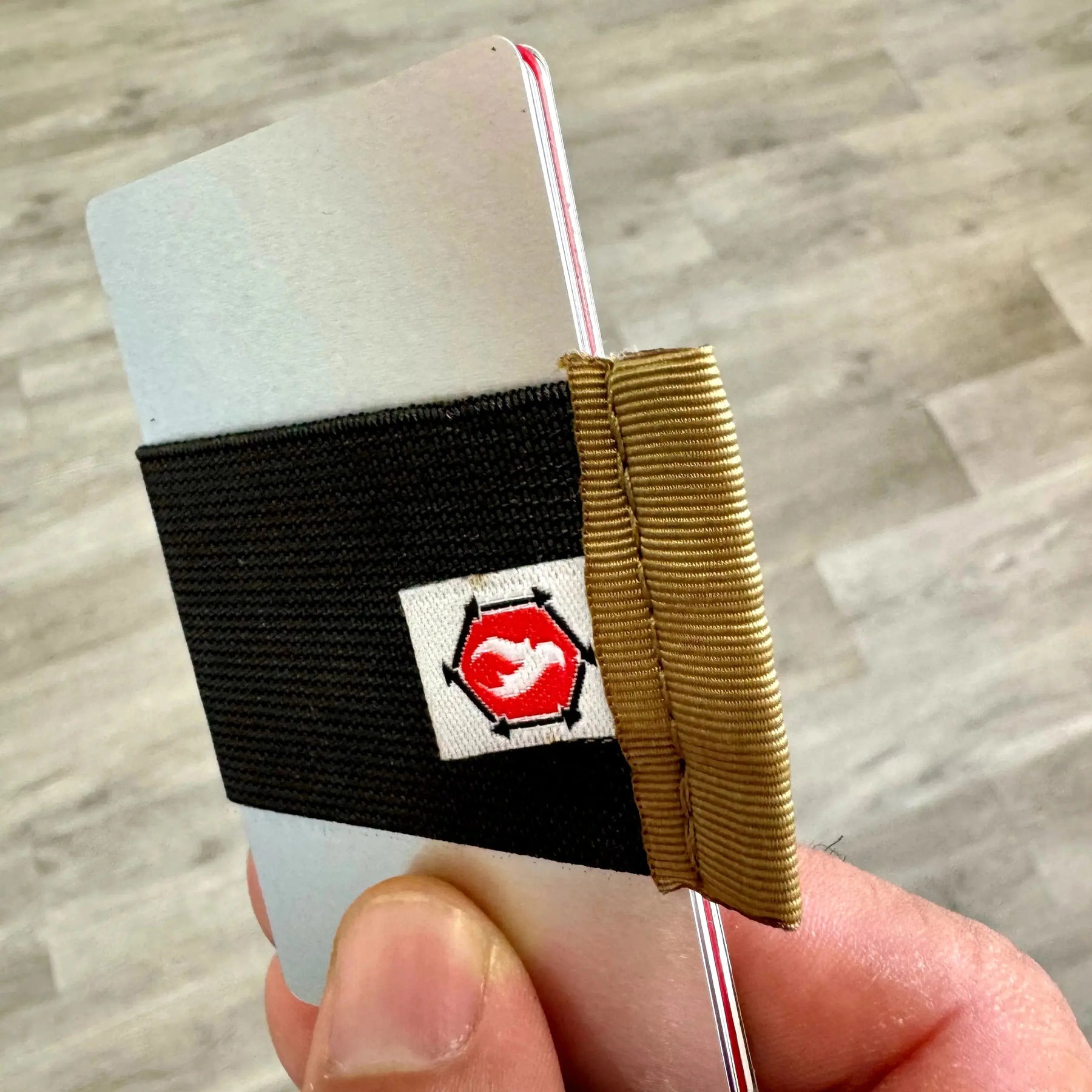 Hand holds aluminum RFID blocker card with black elastic band and red hexagon logo.