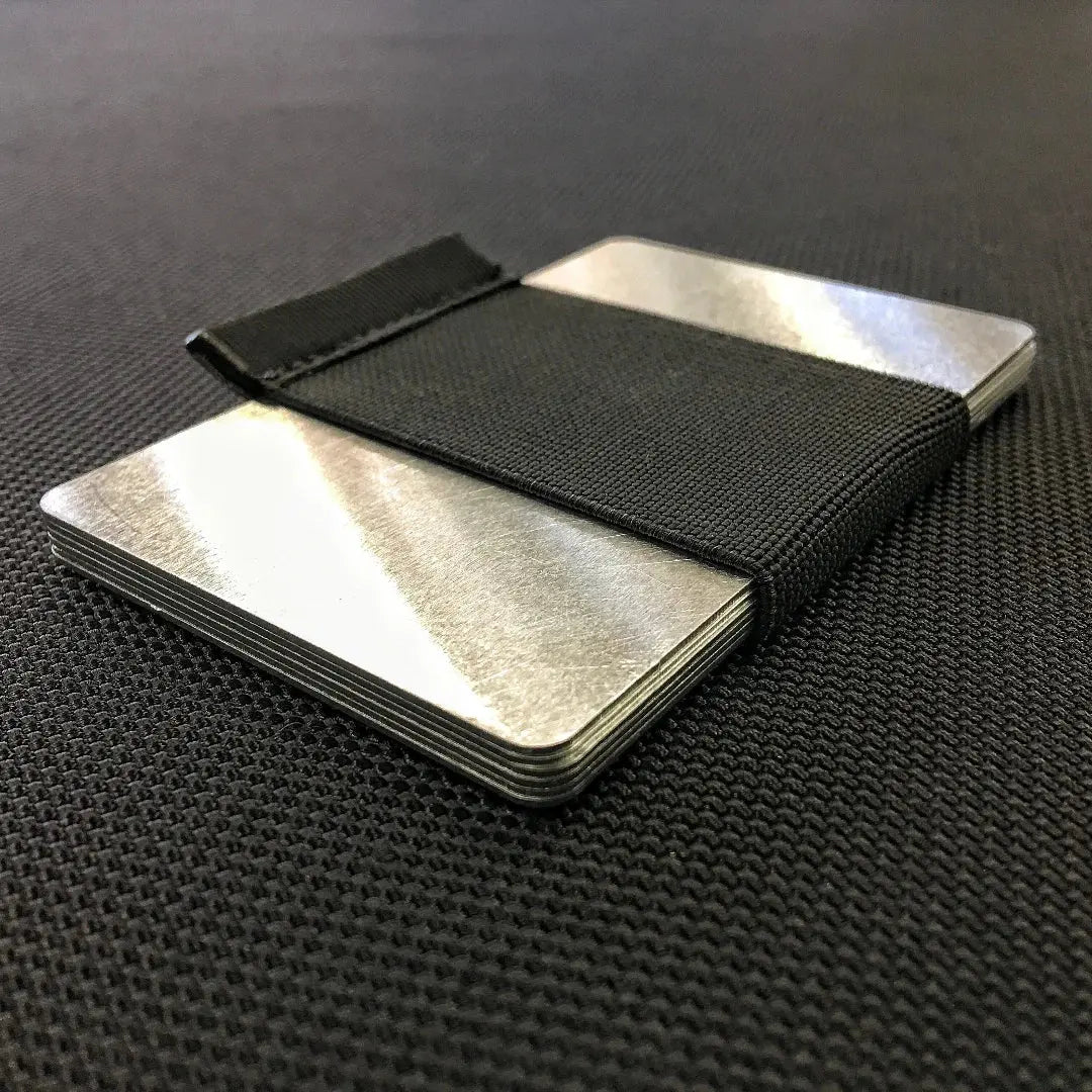 Aluminum RFID blocker card with black elastic band on textured surface.