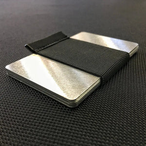 Aluminum RFID blocker card with black elastic band on textured surface.