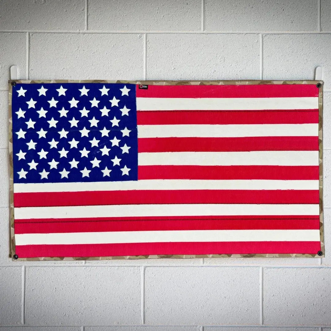 American flag with blue union, white stars, and red and white stripes on a camouflage border.