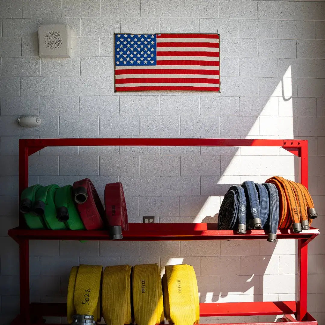 American flag made from red, white, and blue fire hoses on a brick wall.