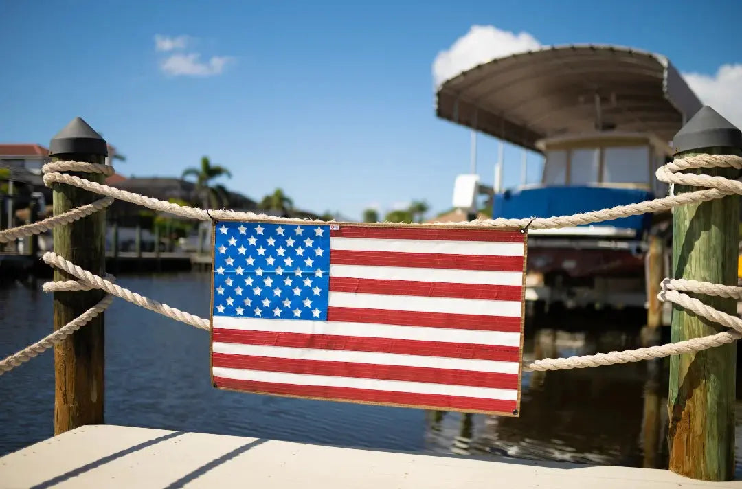 American flag made from red and white striped fire hose hanging on a rope fence.