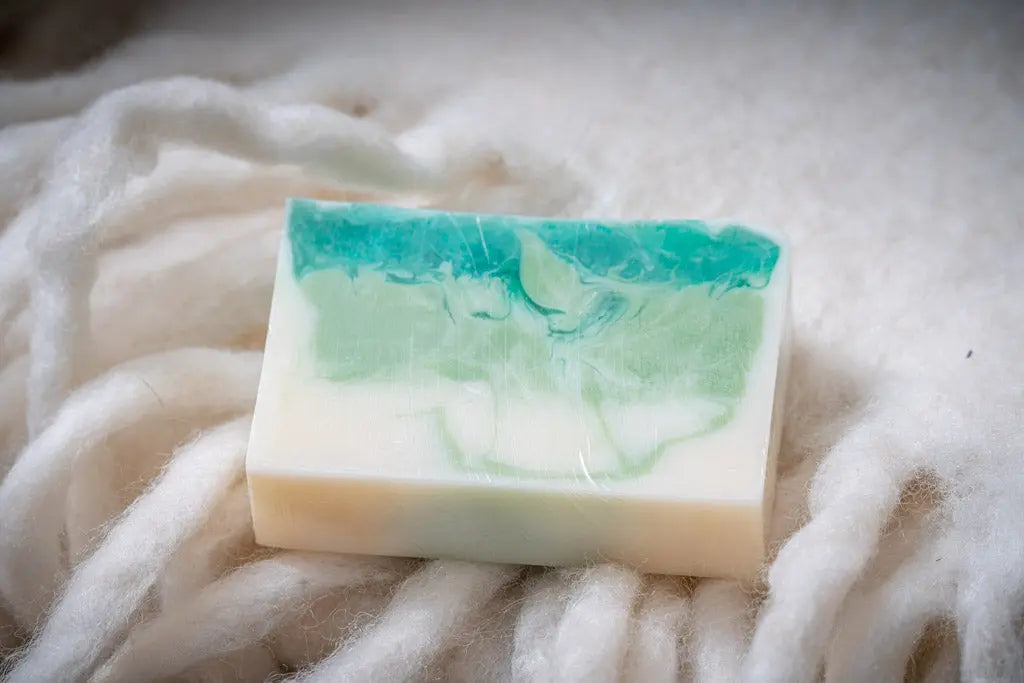 Rectangular bar of layered green and white goats milk soap on a white fuzzy surface.