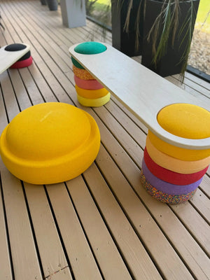 Wooden balance board on top of colorful stacking play stones.