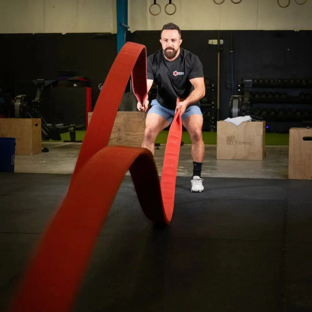 Man using a red 30ft Cadet Cord battle rope in a gym.