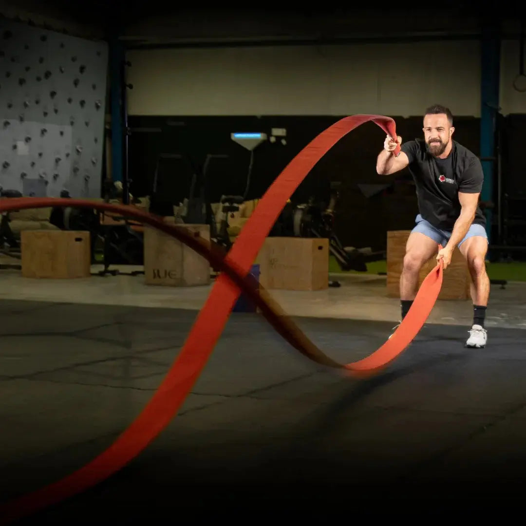 Man using a red battle rope during an exercise in a gym.