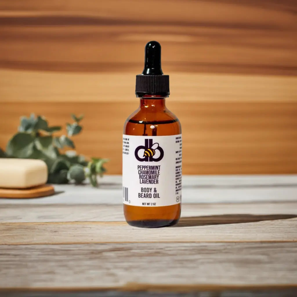 Body & Beard Oil: Peppermint, Chamomile, Rosemary, Lavender. Oil in an amber glass bottle with a black dropper on wooden table.