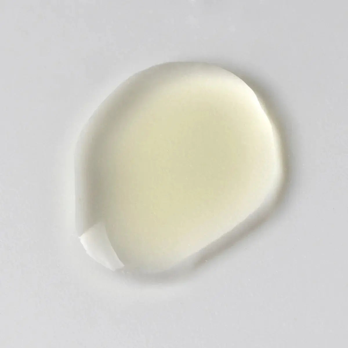 Drop of facial serum. Clear skincare oil on a white surface.