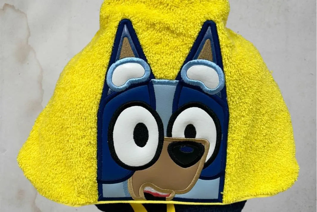 Yellow hooded towel with a cartoon blue dog face, featuring big eyes and dog ears.