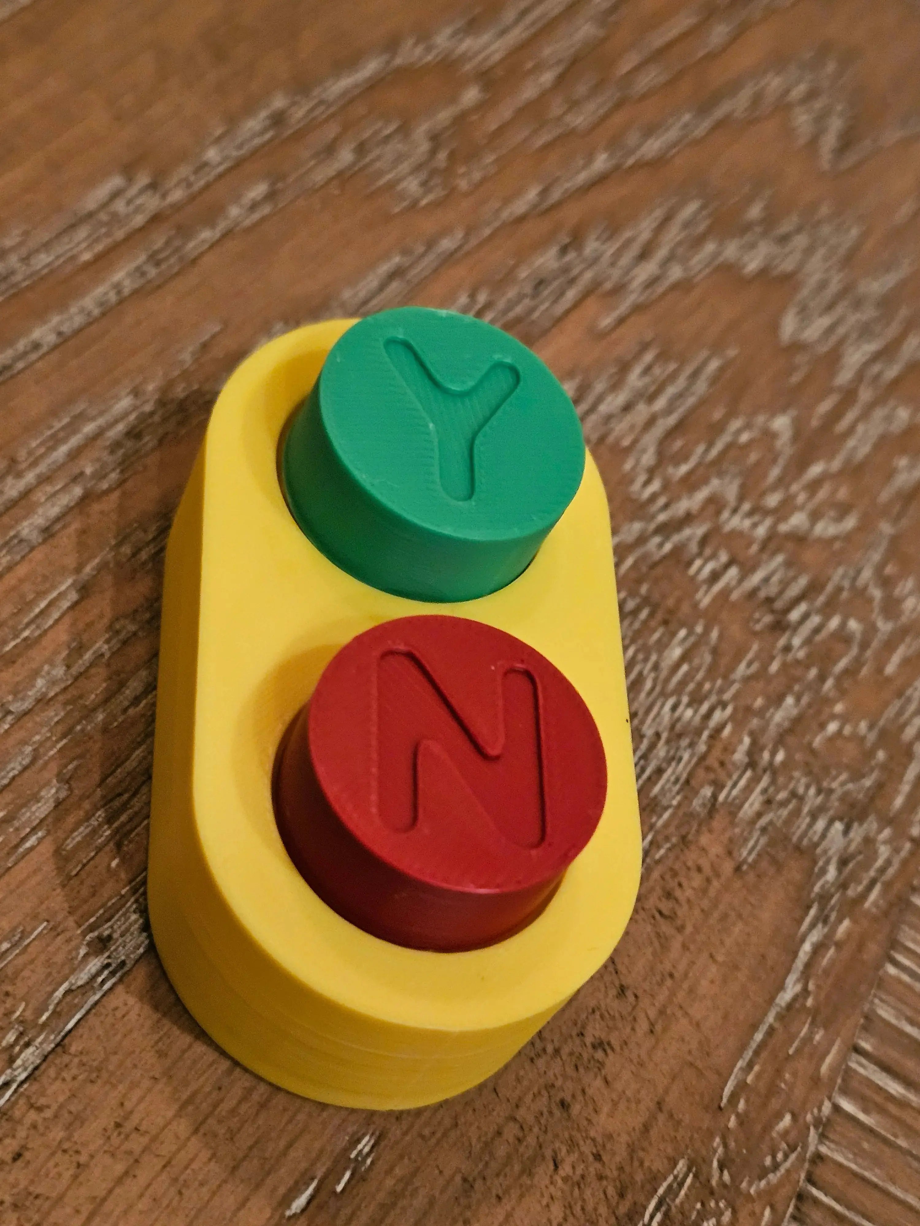 Yellow fidget toy with red 'N' and green 'Y' buttons on a wood surface.