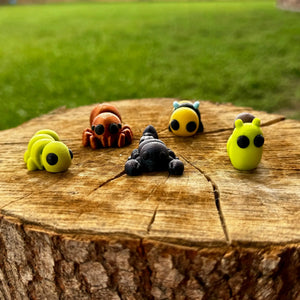 Mushroom Lady Co. Bug Buddies: 3D printed bee, spider, snail, and caterpillar fidget toys on a tree stump.