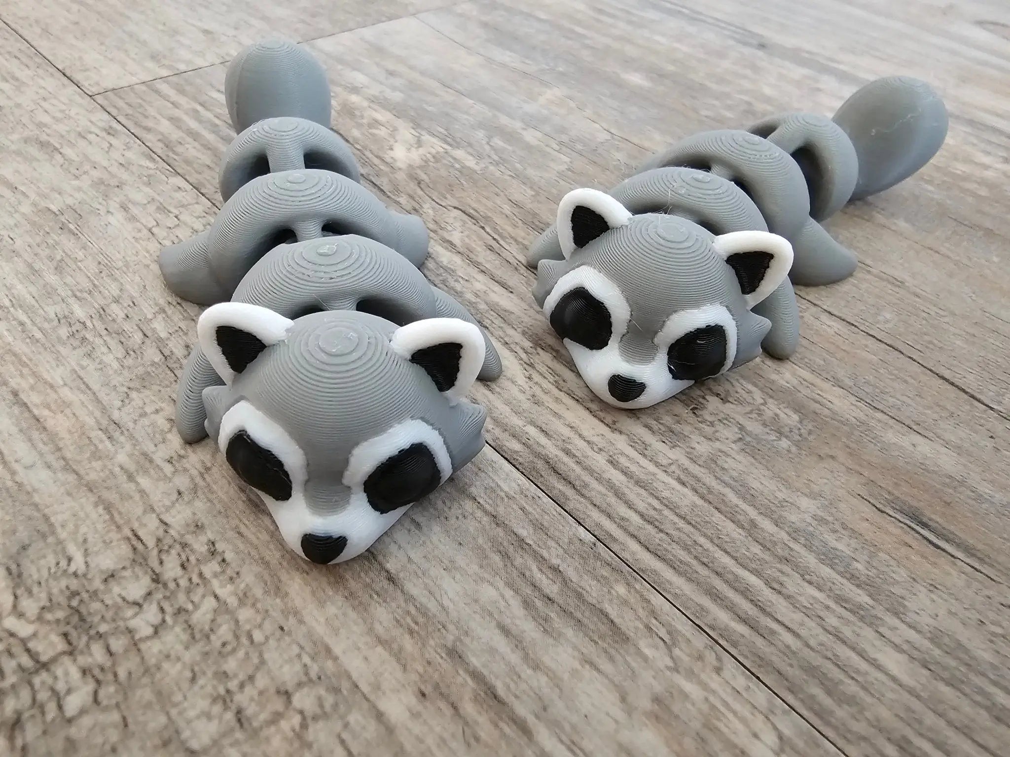 3D Printed Gray Raccoon Fidget Toys on Wood. Cute animal toys for kids, desk pets, fidgets from The Tween Space.