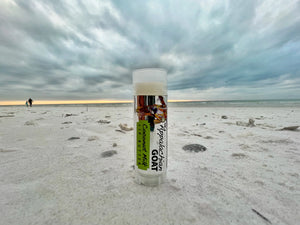 Appalachian Goat Coconut Milk Lip Butter tube on a sandy beach with cloudy sky.