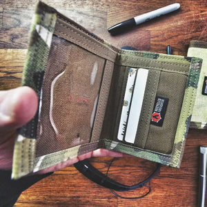 Open camouflage wallet with cards and a black marker on a wooden surface.