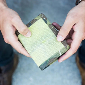 Person holding a bi-fold wallet with multi-camouflaged canvas exterior