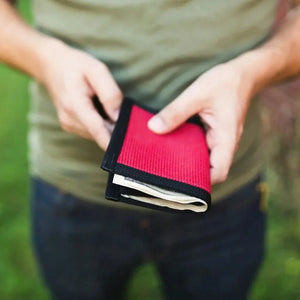 Red fabric wallet with black trim holding cash.