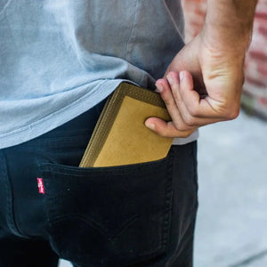 Person putting a brown wallet into the back pocket of black jeans.