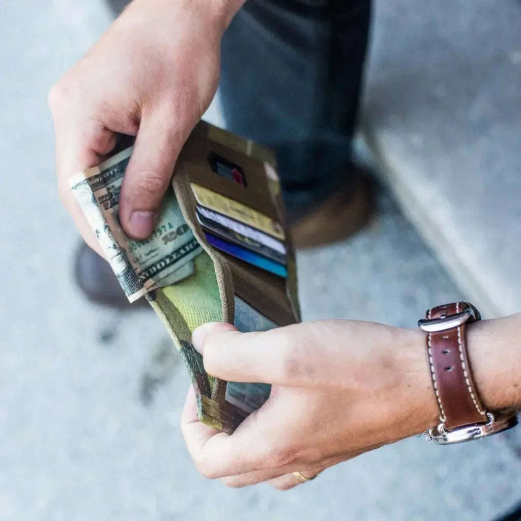 Man's hands holding a bifold wallet with cash and credit cards.