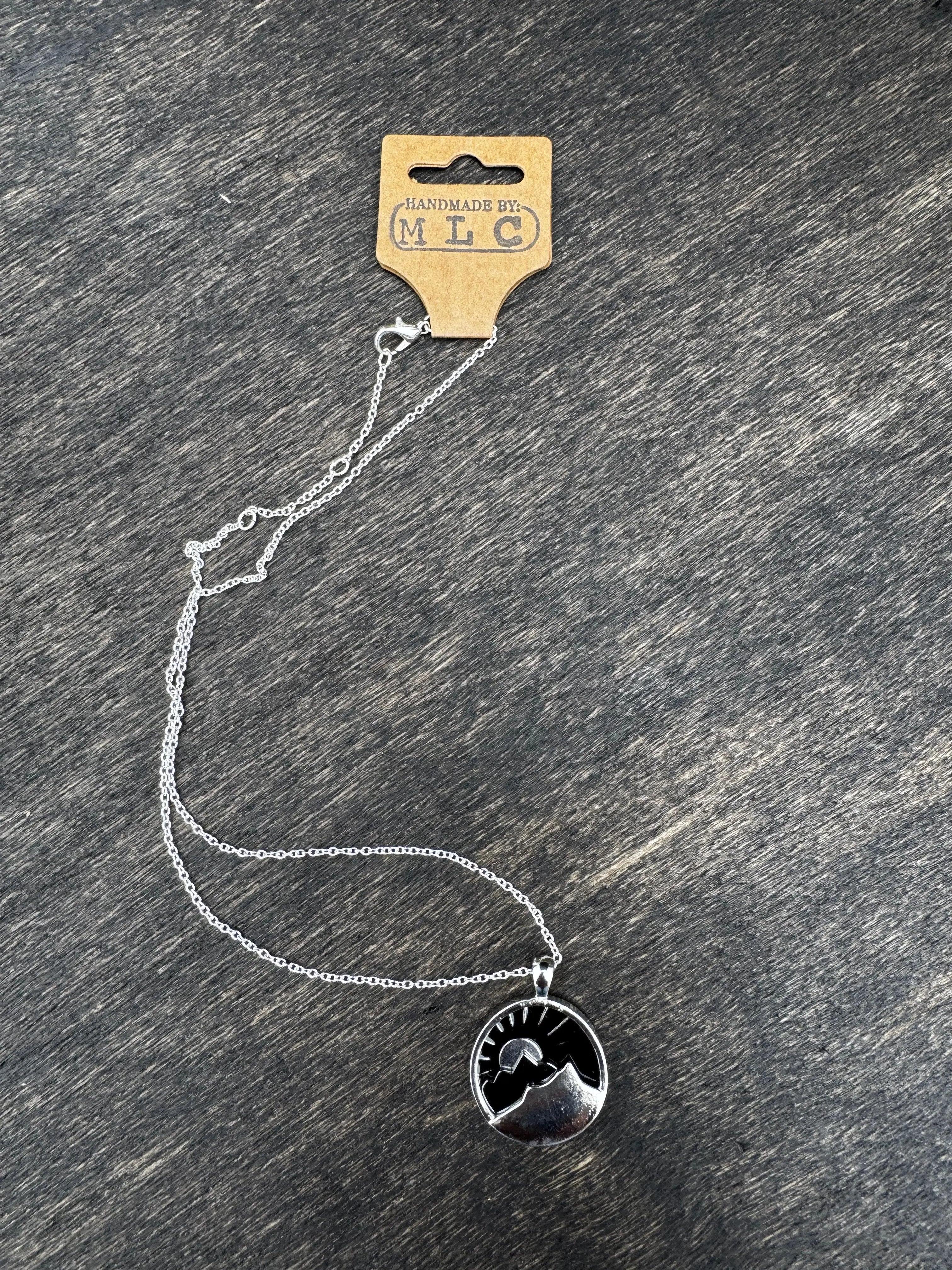 Silver mountain necklace with sun pendant, handmade tag visible, on a dark wood surface. 16 inch chain.