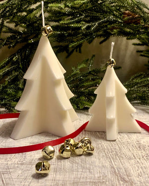 White Christmas tree candles with gold bells and red ribbon on a wooden surface near pine garland.