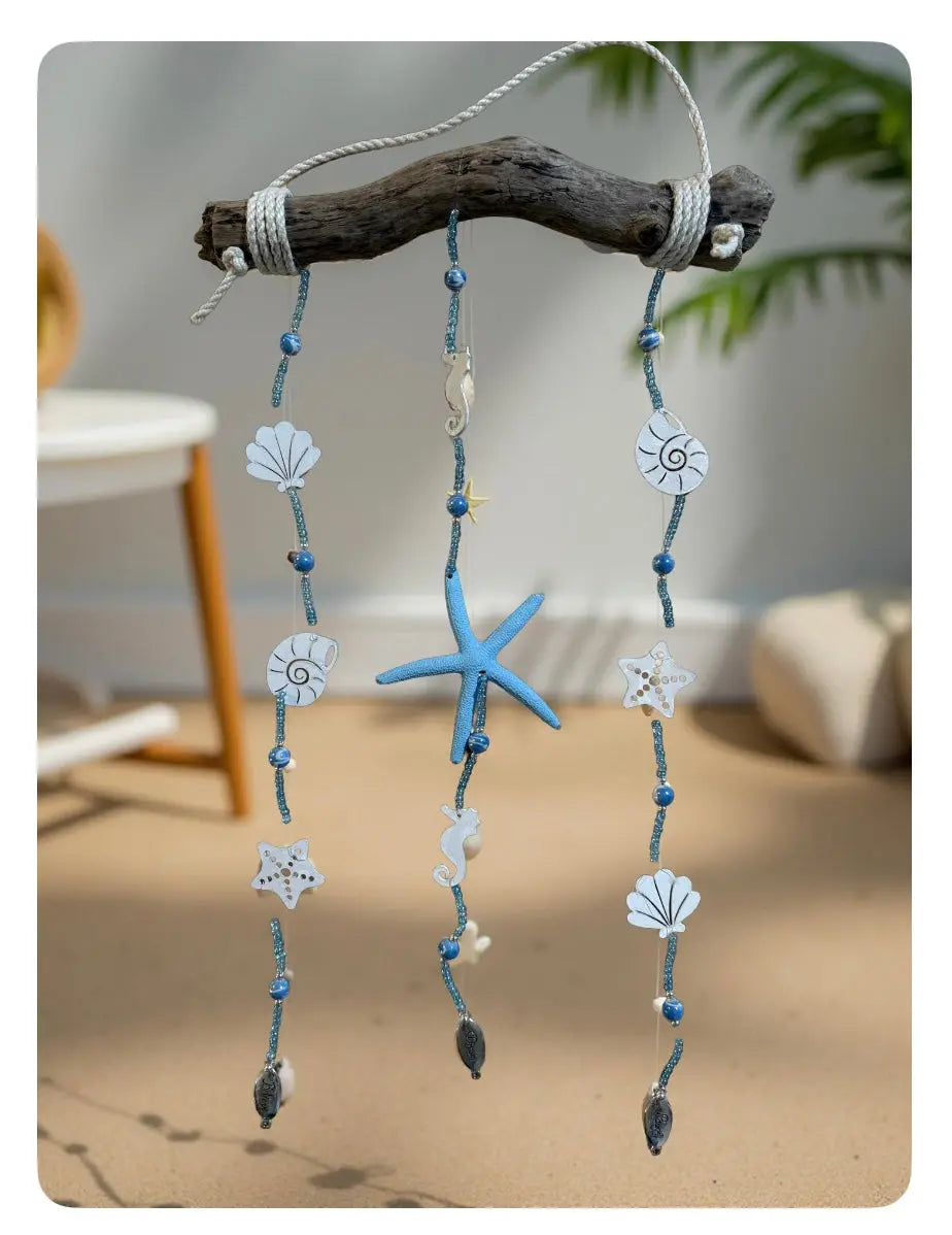 Coastal-themed driftwood hanging decoration with shells, starfish, beads, and rope accents.