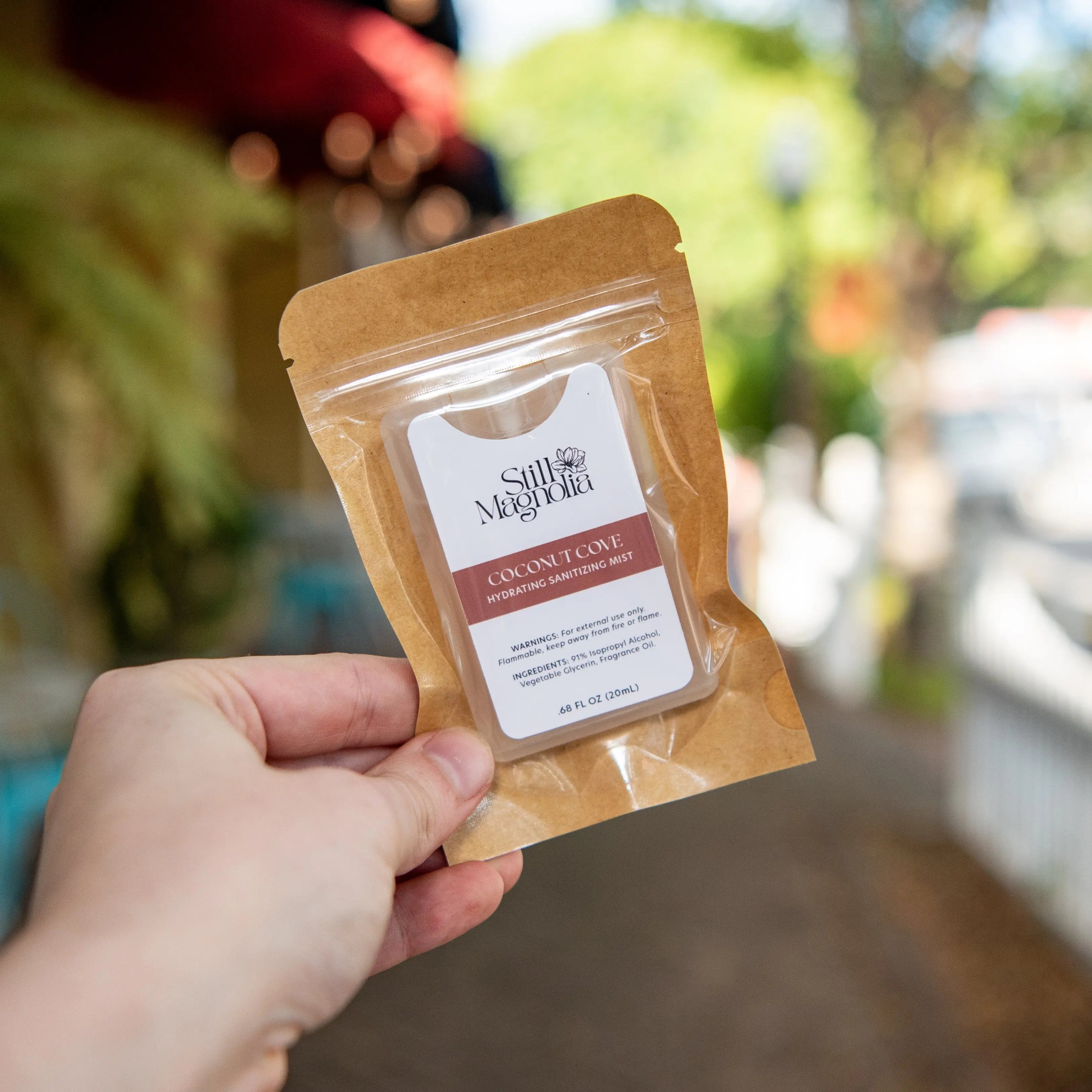 Hand holding a Still Magnolia Coconut Cove hydrating sanitizing mist card.