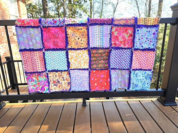 Colorful rag quilt throw with cotton patchwork and fleece backing on a deck railing.