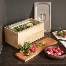 Magnolia wood compost bin with stainless steel interior on a kitchen counter with radishes and herbs.