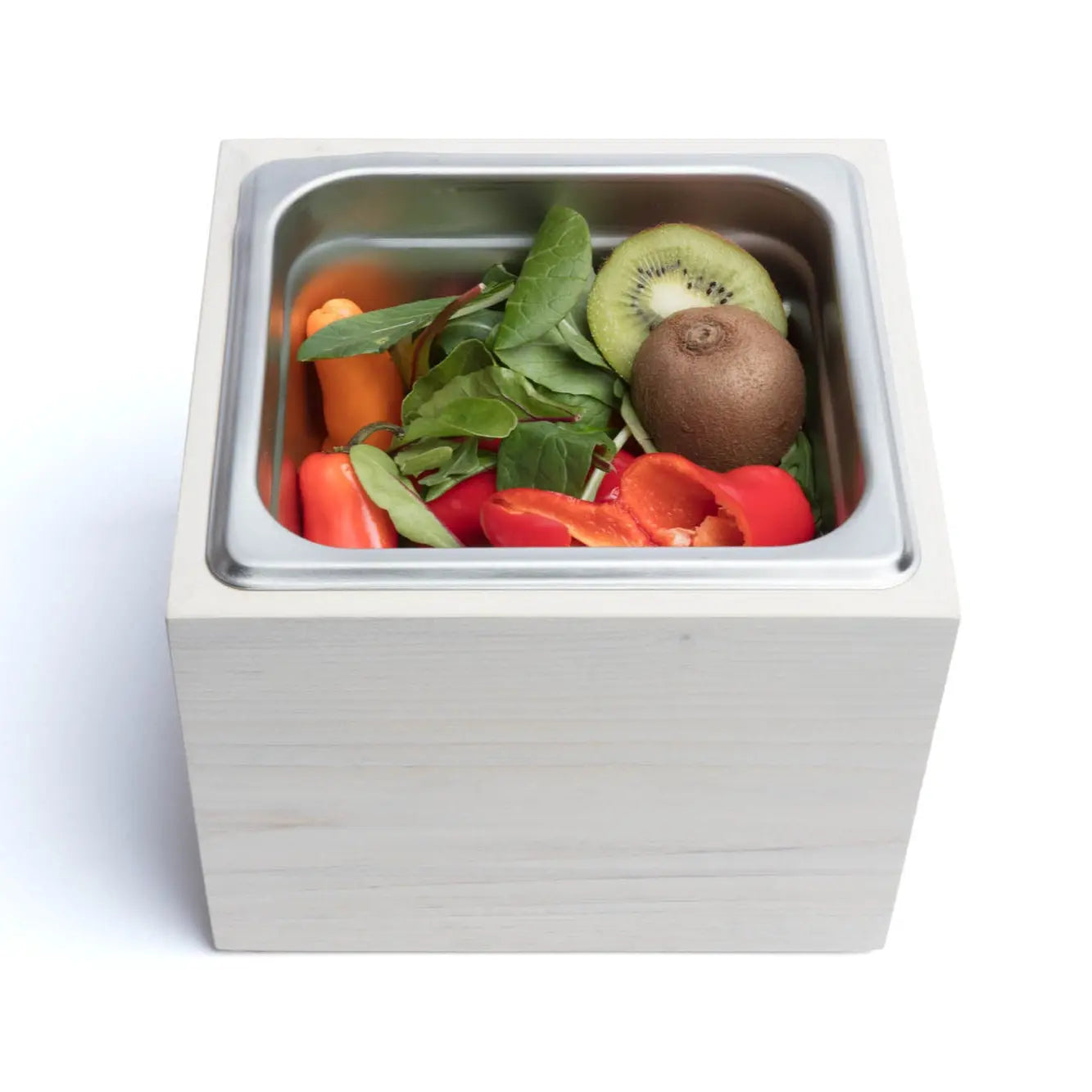 Magnolia wood countertop compost bin with stainless steel insert holding kiwi, peppers, and spinach.