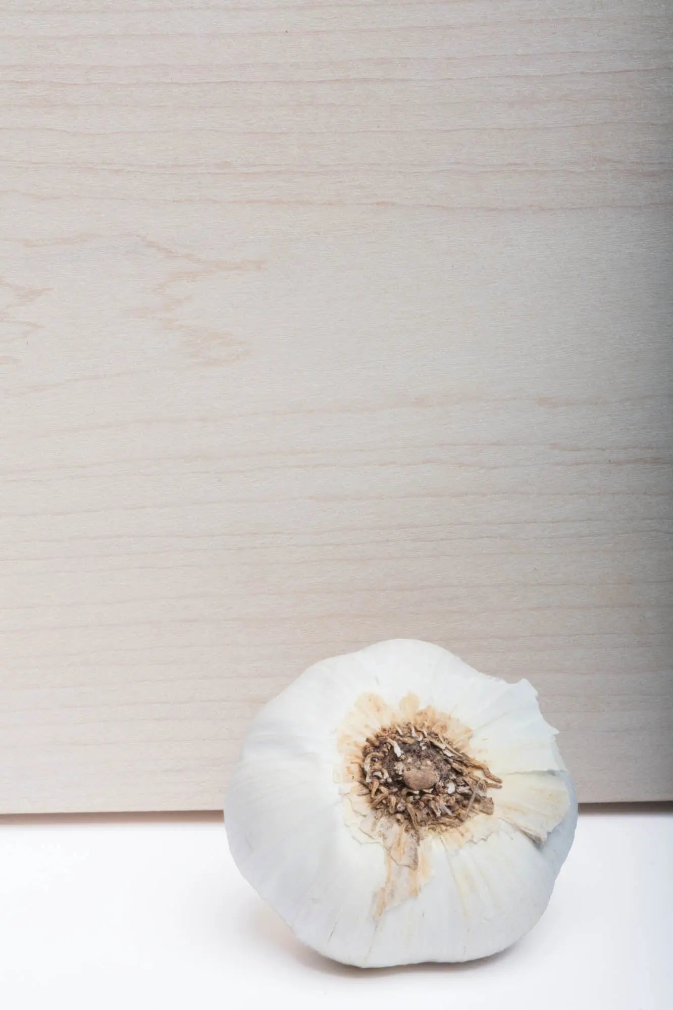 Close-up of a whole garlic bulb on a white countertop against a light wood panel background.