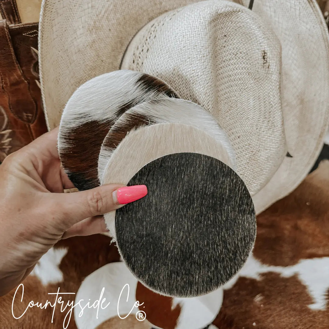 Cowhide coasters, set of 4, rustic western style, on straw hat background.