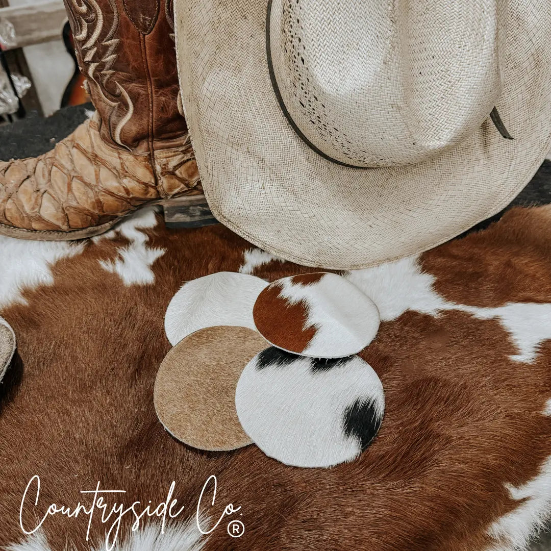 Set of four round cowhide coasters with brown, white, and black patterns.