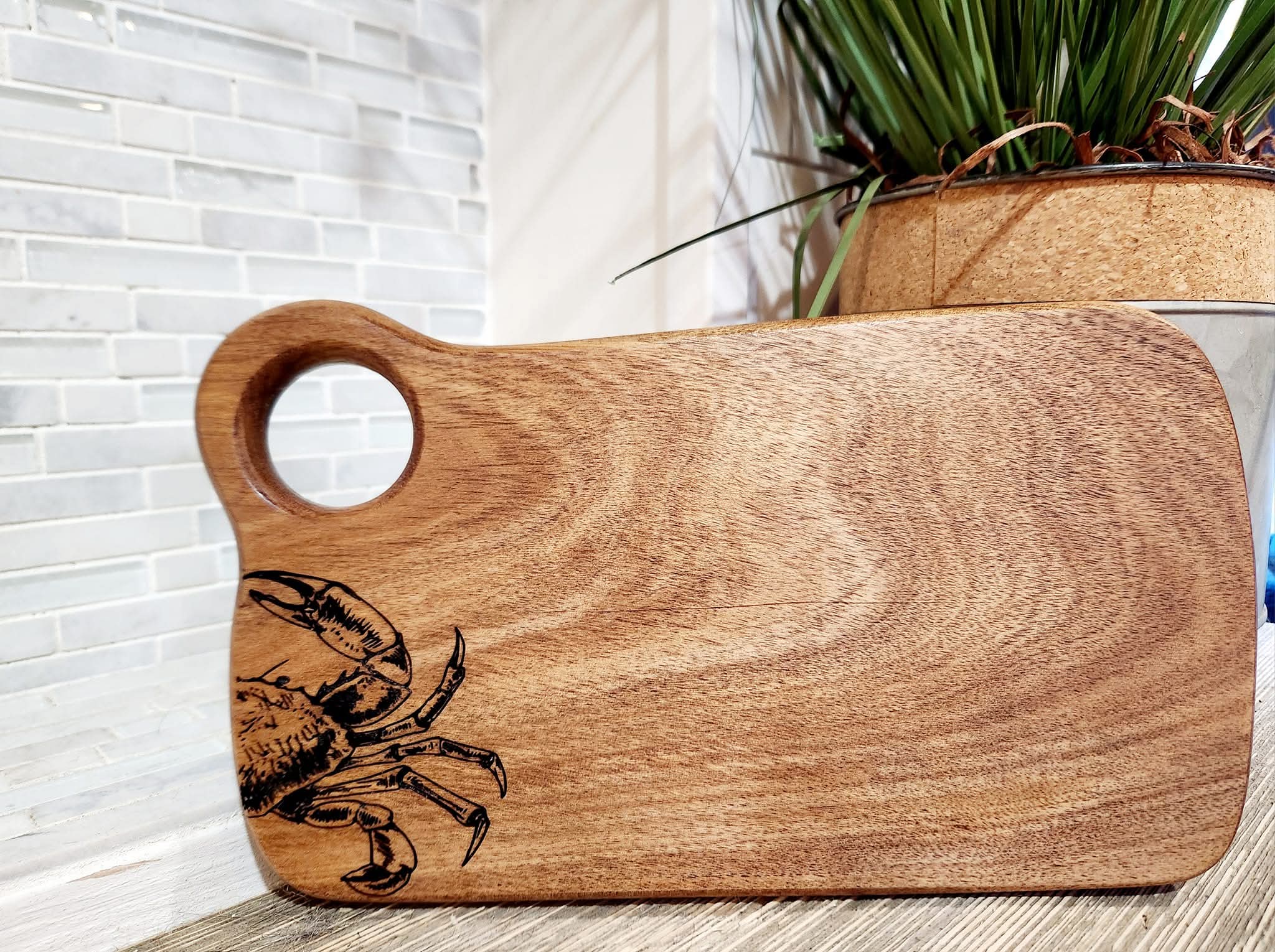 Wooden cutting board with a crab design, round handle, and a light brown wood grain.