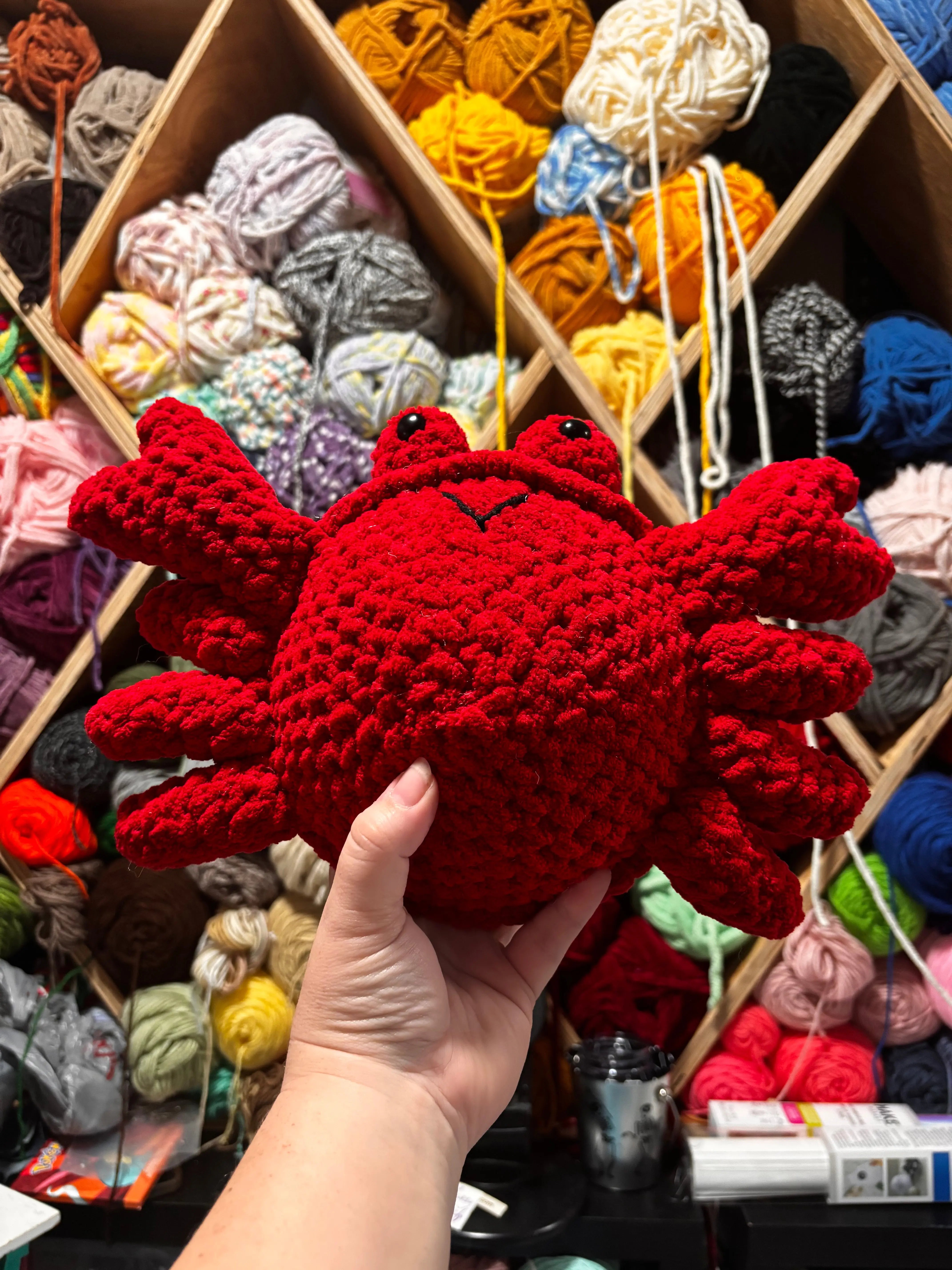 Handmade Red Crocheted Crab Toy by Main Street Collective against colorful yarn stash. Cute Amigurumi Crab