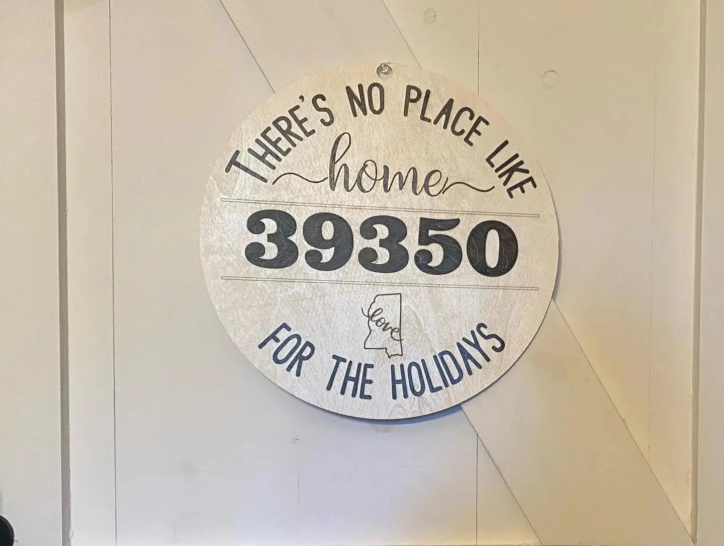 Round wood sign with "There's No Place Like Home" and zip code 39350.