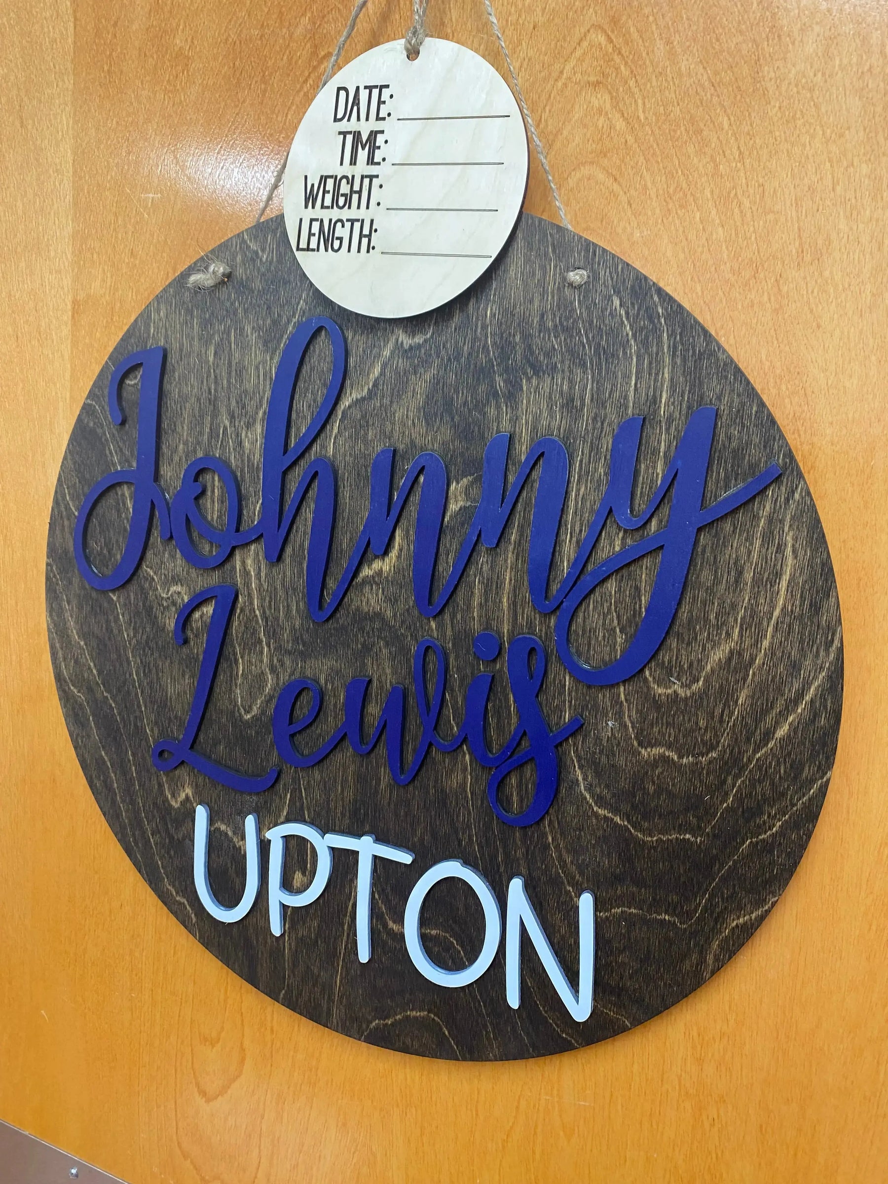Round wood baby name sign with "Johnny Lewis Upton" and birth detail section.