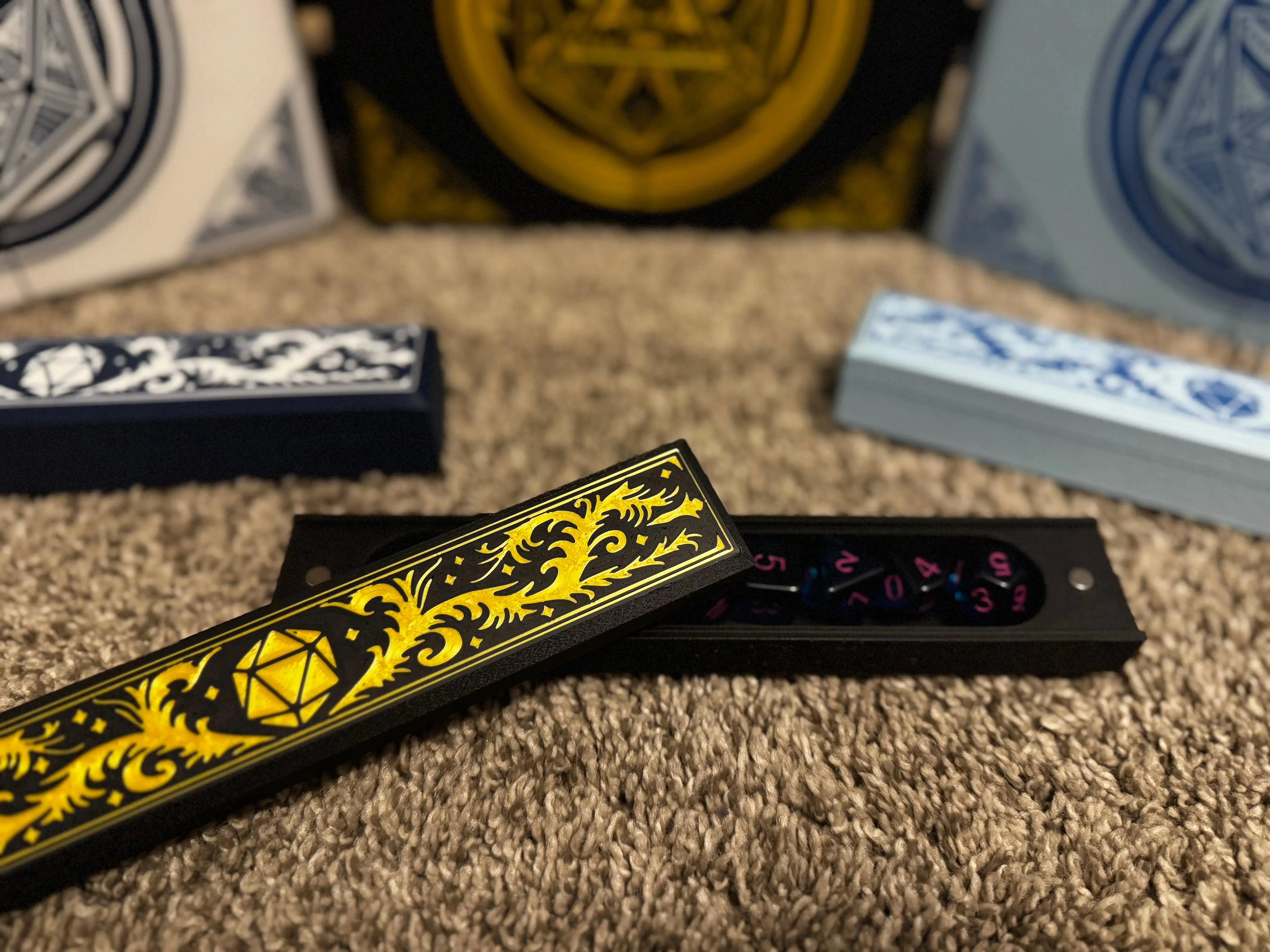 A 3D printed dice box with a yellow design on black, open to show dice inside, resting on a carpet.