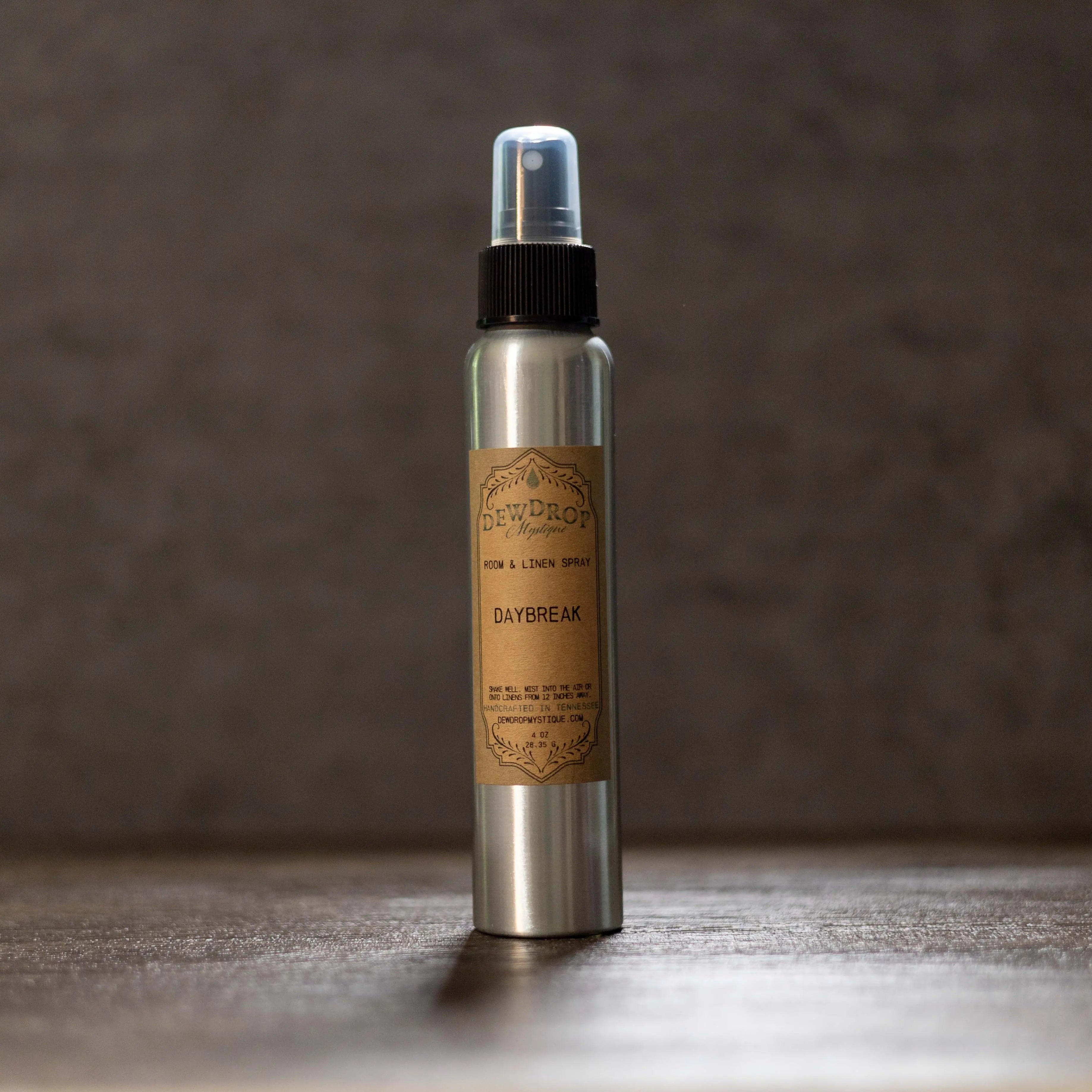 Dewdrop Mystique Daybreak Room and Linen Spray in a silver bottle with a brown label.