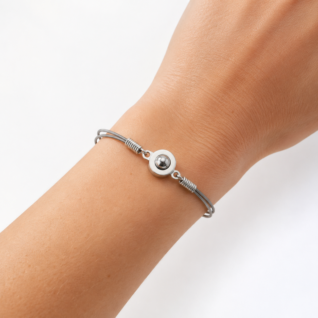 Silver bracelet with a round charm on a wrist against a white background
