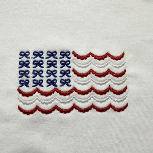 White cotton tank top with embroidered blue bows and red and white wavy stripes resembling an American flag.